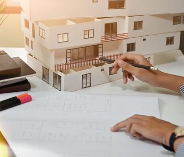 Female architect working with model house and blueprint in home office.